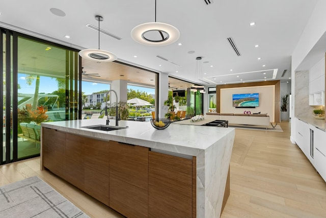 kitchen with modern cabinets, a sink, brown cabinetry, a wall of windows, and a large island with sink