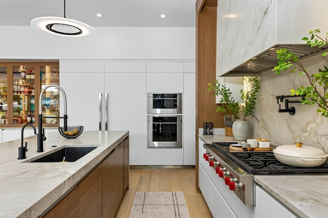 kitchen featuring wall chimney range hood, modern cabinets, stainless steel appliances, and a sink