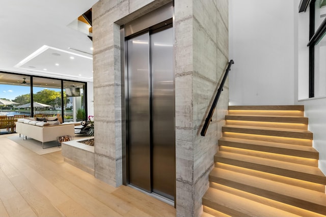 stairs featuring expansive windows, elevator, and wood finished floors