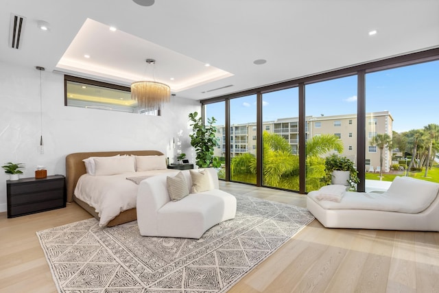 bedroom featuring a raised ceiling, floor to ceiling windows, visible vents, and light wood finished floors