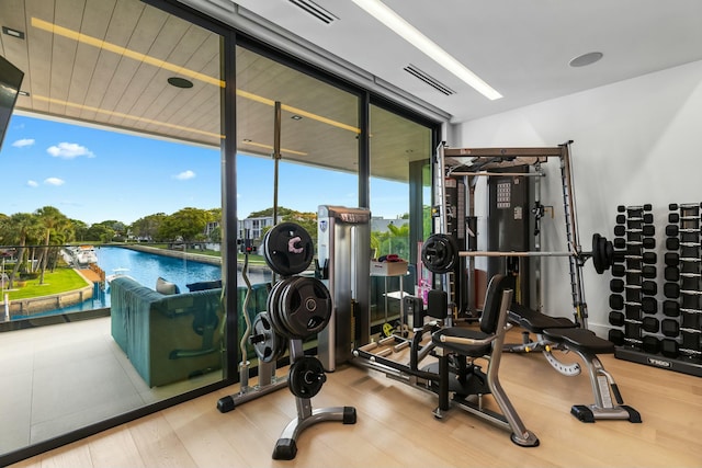 workout area with a wall of windows, wood finished floors, visible vents, and a water view