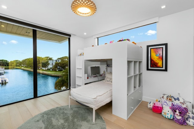 bedroom featuring floor to ceiling windows, wood finished floors, and a water view