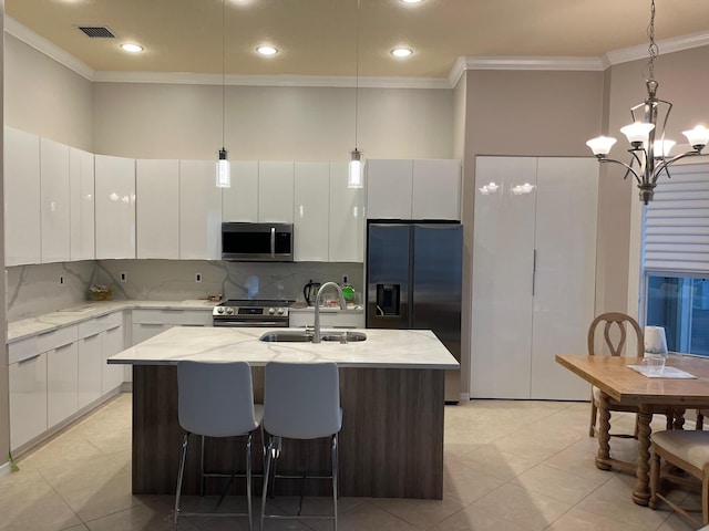 kitchen with appliances with stainless steel finishes, an island with sink, a sink, and white cabinetry