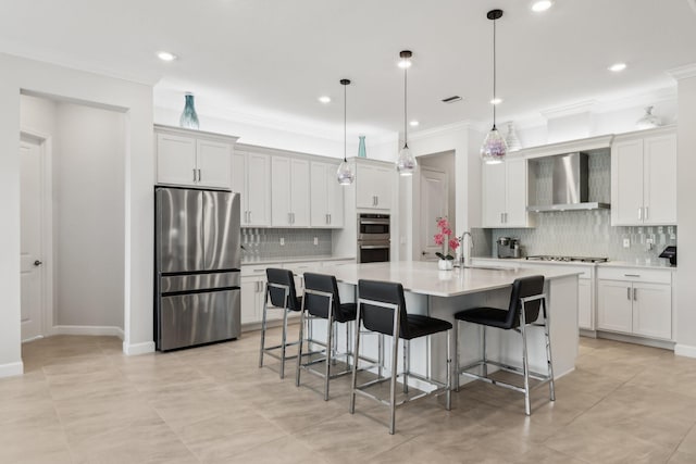 kitchen featuring appliances with stainless steel finishes, a kitchen bar, hanging light fixtures, a center island with sink, and wall chimney range hood