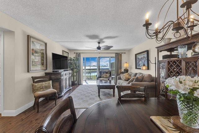 living room with dark wood-type flooring, ceiling fan with notable chandelier, and a textured ceiling