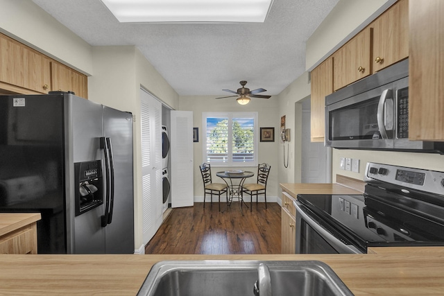 kitchen with a textured ceiling, appliances with stainless steel finishes, dark hardwood / wood-style floors, ceiling fan, and stacked washer / dryer