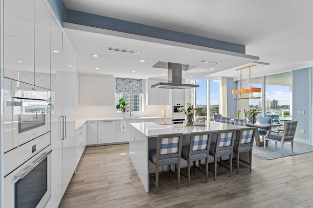 kitchen featuring light hardwood / wood-style flooring, white cabinetry, a center island, island range hood, and decorative light fixtures