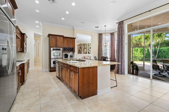 kitchen with light tile patterned floors, appliances with stainless steel finishes, light stone counters, an island with sink, and decorative light fixtures