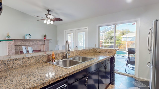 kitchen with stainless steel refrigerator, plenty of natural light, light stone countertops, and sink