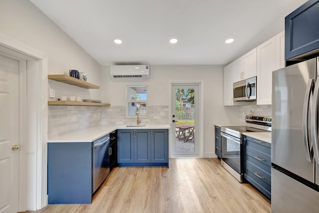 kitchen with a wall mounted air conditioner, light countertops, appliances with stainless steel finishes, blue cabinets, and a sink