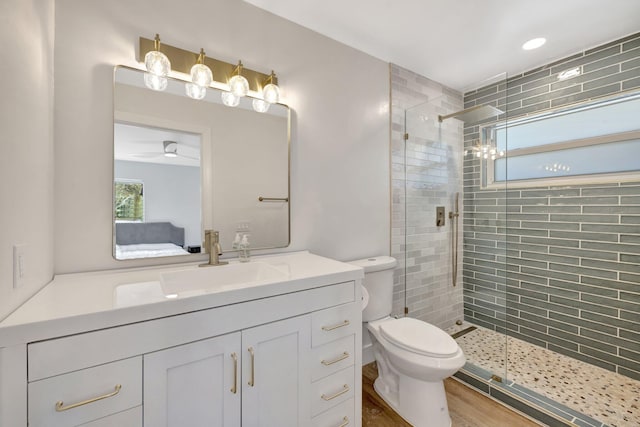 bathroom featuring toilet, a tile shower, wood finished floors, vanity, and a ceiling fan