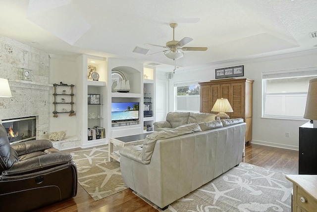 living room featuring built in shelves, ceiling fan, wood-type flooring, and a fireplace