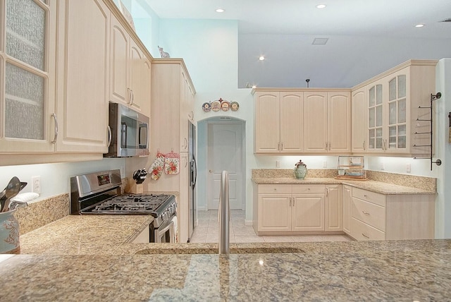 kitchen with light stone counters, appliances with stainless steel finishes, a high ceiling, and light tile patterned floors