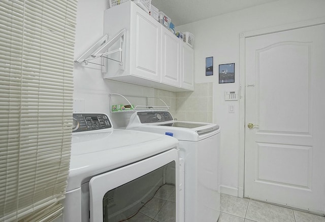 clothes washing area featuring light tile patterned floors, cabinets, and washing machine and clothes dryer