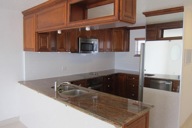 kitchen featuring appliances with stainless steel finishes, sink, backsplash, dark stone counters, and kitchen peninsula