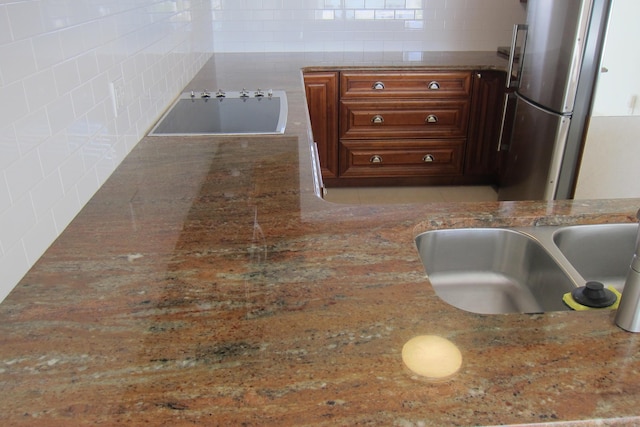 interior details featuring stone counters, sink, and stainless steel refrigerator