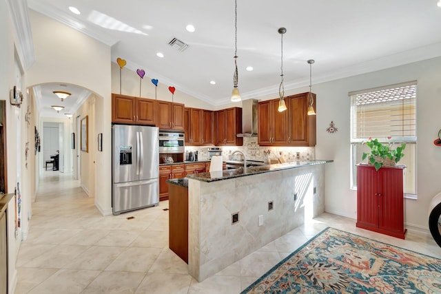 kitchen with pendant lighting, dark stone counters, ornamental molding, stainless steel appliances, and wall chimney range hood