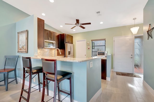 kitchen with tasteful backsplash, a kitchen breakfast bar, kitchen peninsula, pendant lighting, and stainless steel appliances