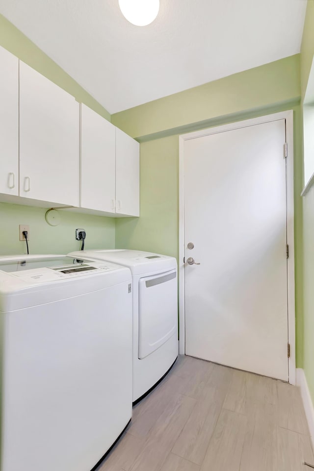 washroom featuring cabinets, washing machine and clothes dryer, and light hardwood / wood-style flooring