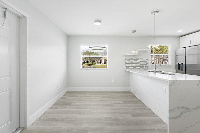 kitchen with sink, light hardwood / wood-style flooring, stainless steel refrigerator with ice dispenser, white cabinets, and decorative light fixtures