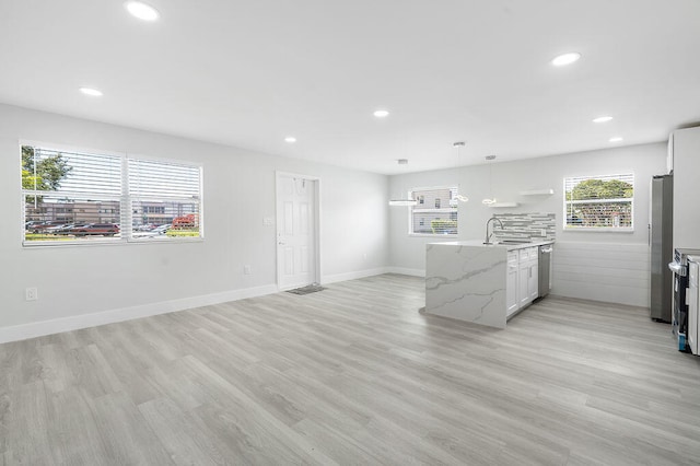 kitchen with sink, hanging light fixtures, light stone counters, white cabinets, and light wood-type flooring