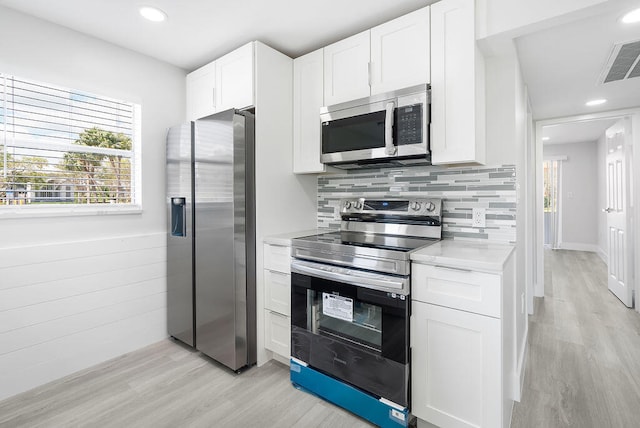 kitchen with tasteful backsplash, appliances with stainless steel finishes, light hardwood / wood-style floors, and white cabinets