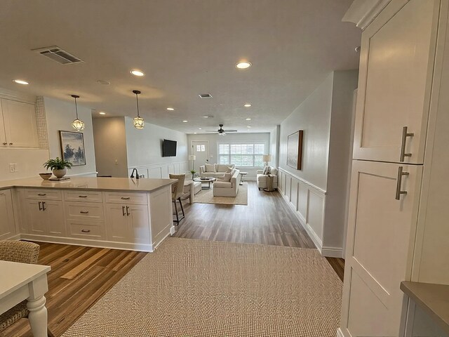 kitchen featuring wood finished floors, a decorative wall, recessed lighting, white cabinetry, and a peninsula