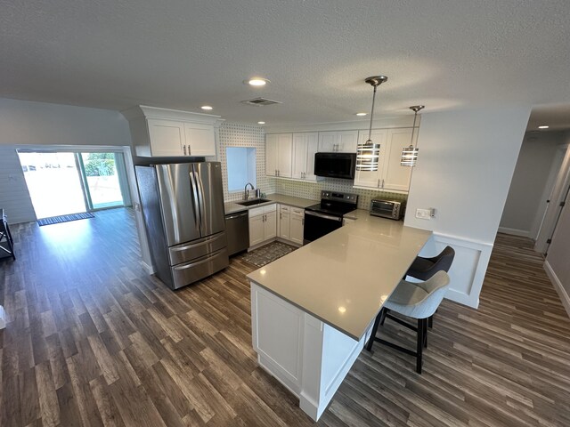 kitchen with white cabinetry, appliances with stainless steel finishes, kitchen peninsula, and hanging light fixtures