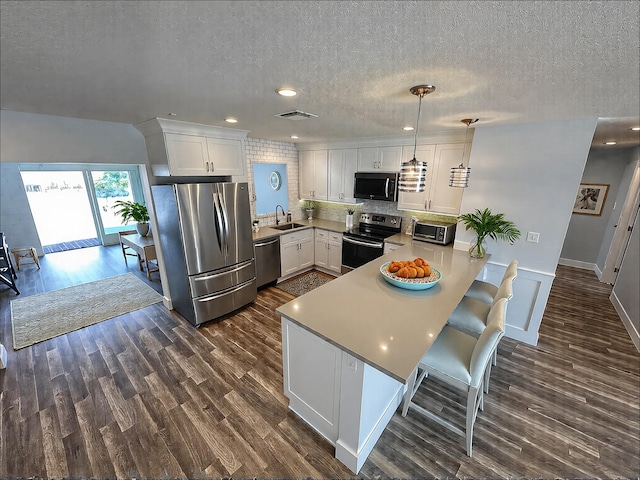 kitchen featuring appliances with stainless steel finishes, a peninsula, a sink, a textured ceiling, and dark wood-style flooring