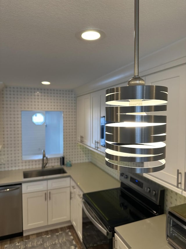 kitchen with a sink, appliances with stainless steel finishes, white cabinetry, light countertops, and a textured ceiling
