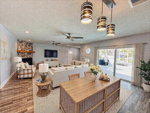 living area with a textured ceiling, wood finished floors, baseboards, a ceiling fan, and a fireplace