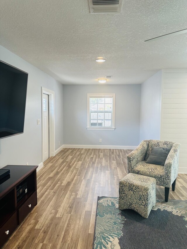 living room featuring ceiling fan, wood-type flooring, a fireplace, and a textured ceiling