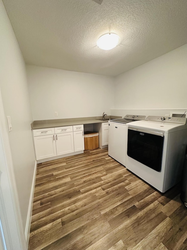 clothes washing area with cabinet space, washing machine and dryer, light wood-style floors, and a textured ceiling