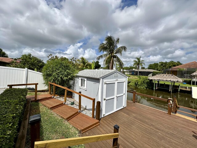 deck featuring a shed, fence, a water view, an outbuilding, and a boat dock