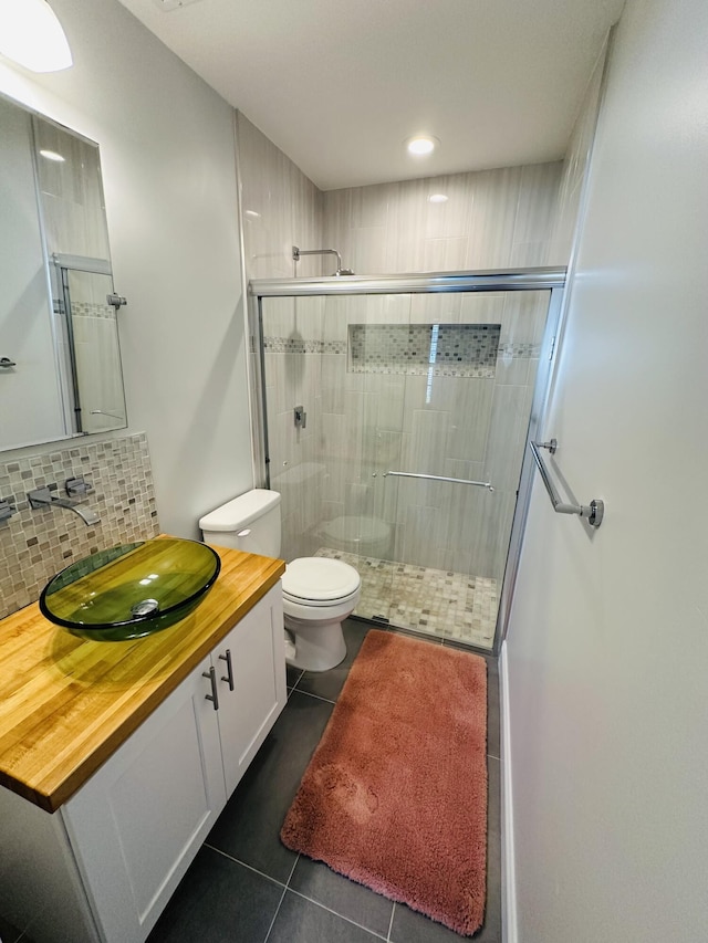 bathroom featuring tile patterned flooring, vanity, tasteful backsplash, an enclosed shower, and toilet