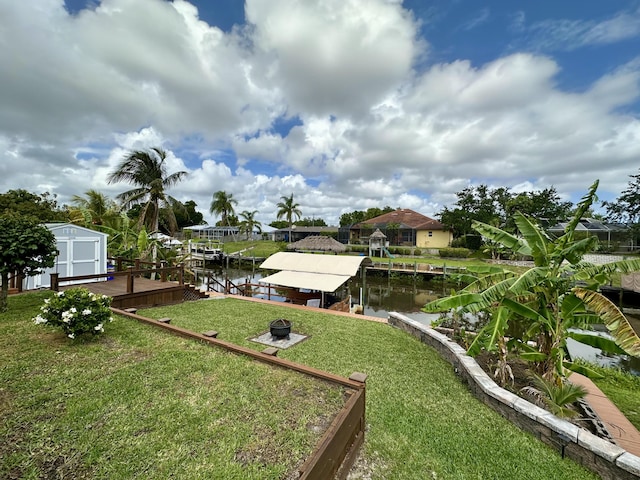 view of grassy yard with boat lift, a boat dock, a shed, a water view, and an outdoor structure