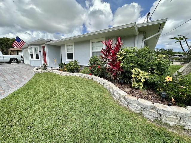 ranch-style home featuring stucco siding, a front yard, and driveway