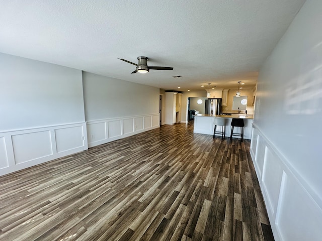 unfurnished living room with a textured ceiling, dark hardwood / wood-style floors, and ceiling fan