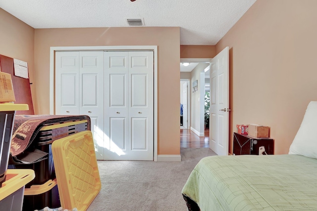 carpeted bedroom with a textured ceiling, a closet, visible vents, and baseboards