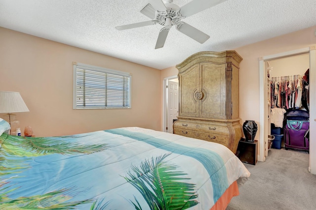 bedroom with a spacious closet, light colored carpet, ceiling fan, a textured ceiling, and a closet