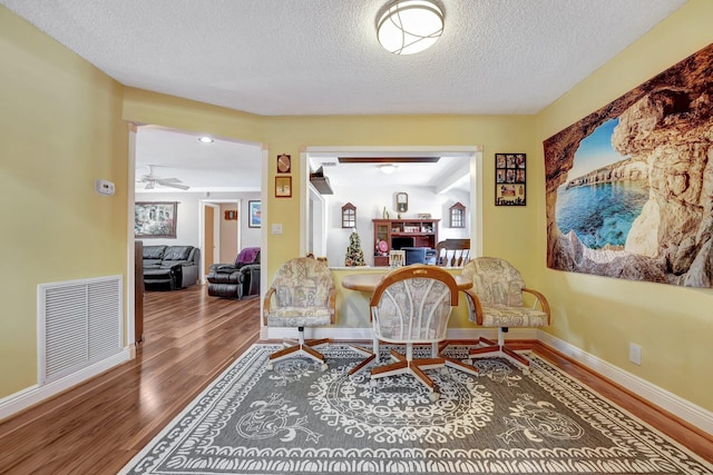 living area with a fireplace, visible vents, a textured ceiling, wood finished floors, and baseboards