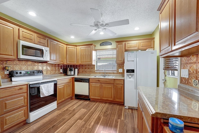 kitchen featuring light wood finished floors, white appliances, a sink, and tasteful backsplash