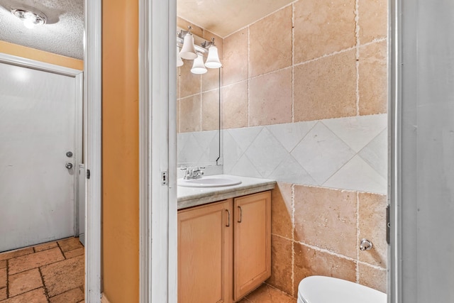 bathroom with vanity, a textured ceiling, toilet, and tile walls