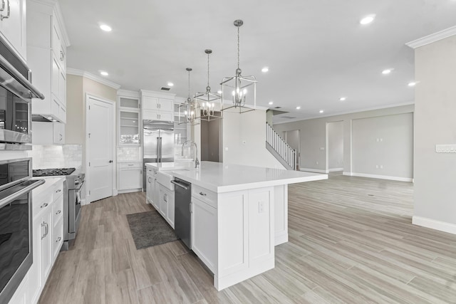 kitchen featuring pendant lighting, high quality appliances, an island with sink, white cabinets, and ornamental molding