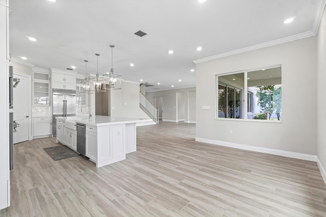 kitchen with sink, appliances with stainless steel finishes, white cabinets, a center island with sink, and decorative light fixtures