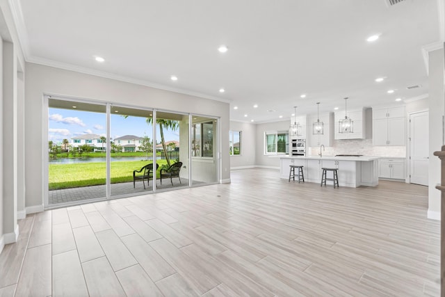 unfurnished living room with crown molding, a water view, sink, and light wood-type flooring