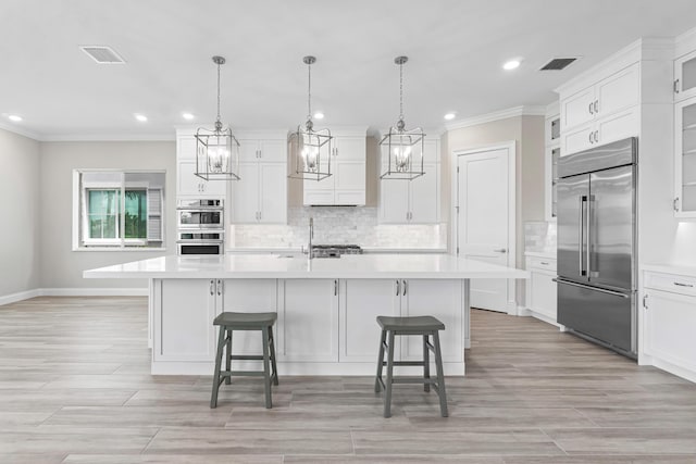 kitchen featuring a kitchen bar, hanging light fixtures, a center island with sink, stainless steel appliances, and white cabinets