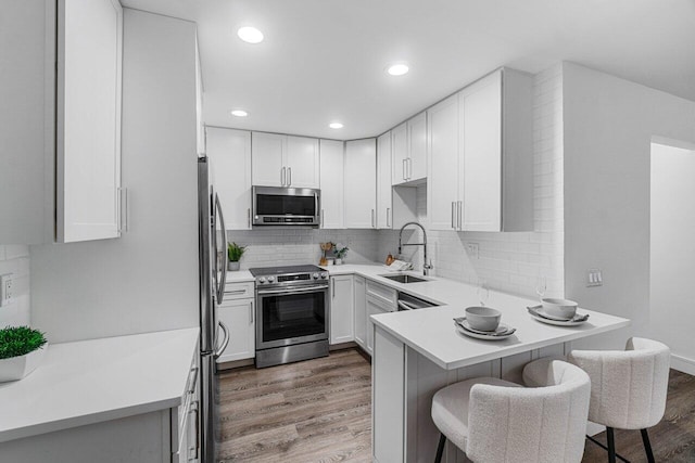 kitchen with a breakfast bar, sink, white cabinetry, hardwood / wood-style flooring, and stainless steel appliances