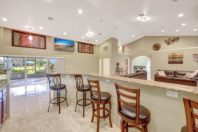 kitchen with a kitchen bar, high vaulted ceiling, hanging light fixtures, light tile patterned floors, and light stone countertops