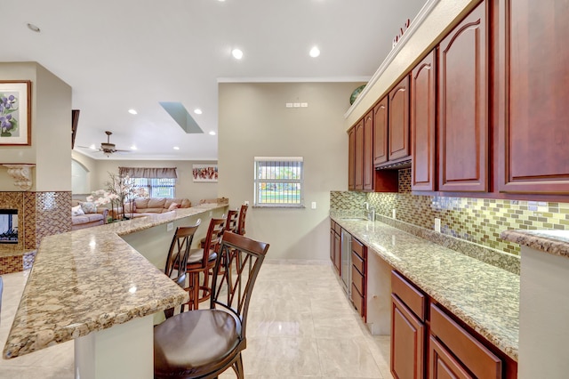 kitchen with a multi sided fireplace, a kitchen breakfast bar, light stone countertops, and decorative backsplash